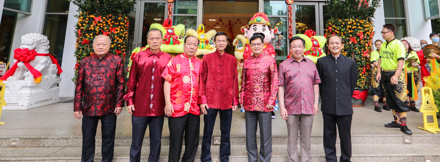 People in traditional Chinese clothing pose with lion dancers and a costumed figure at an event.